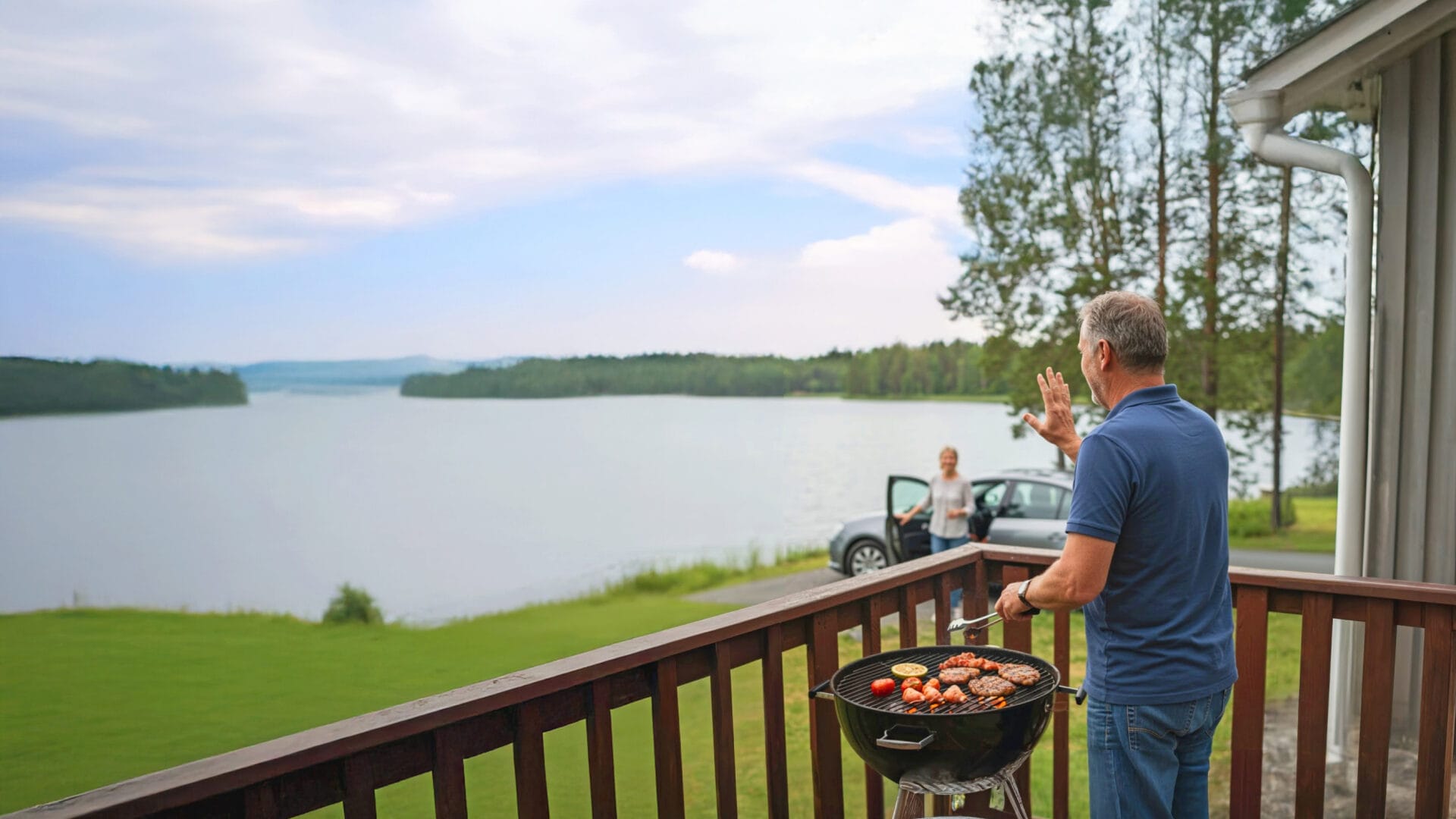 Nainen saapunut autolla mökkipihaan järven rannalle, grillaava mies tervehtii. Lomalla, perillä.