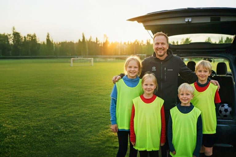 aikuinen neljän nuoren jalkapallon pelaajan kanssa auton vieressä