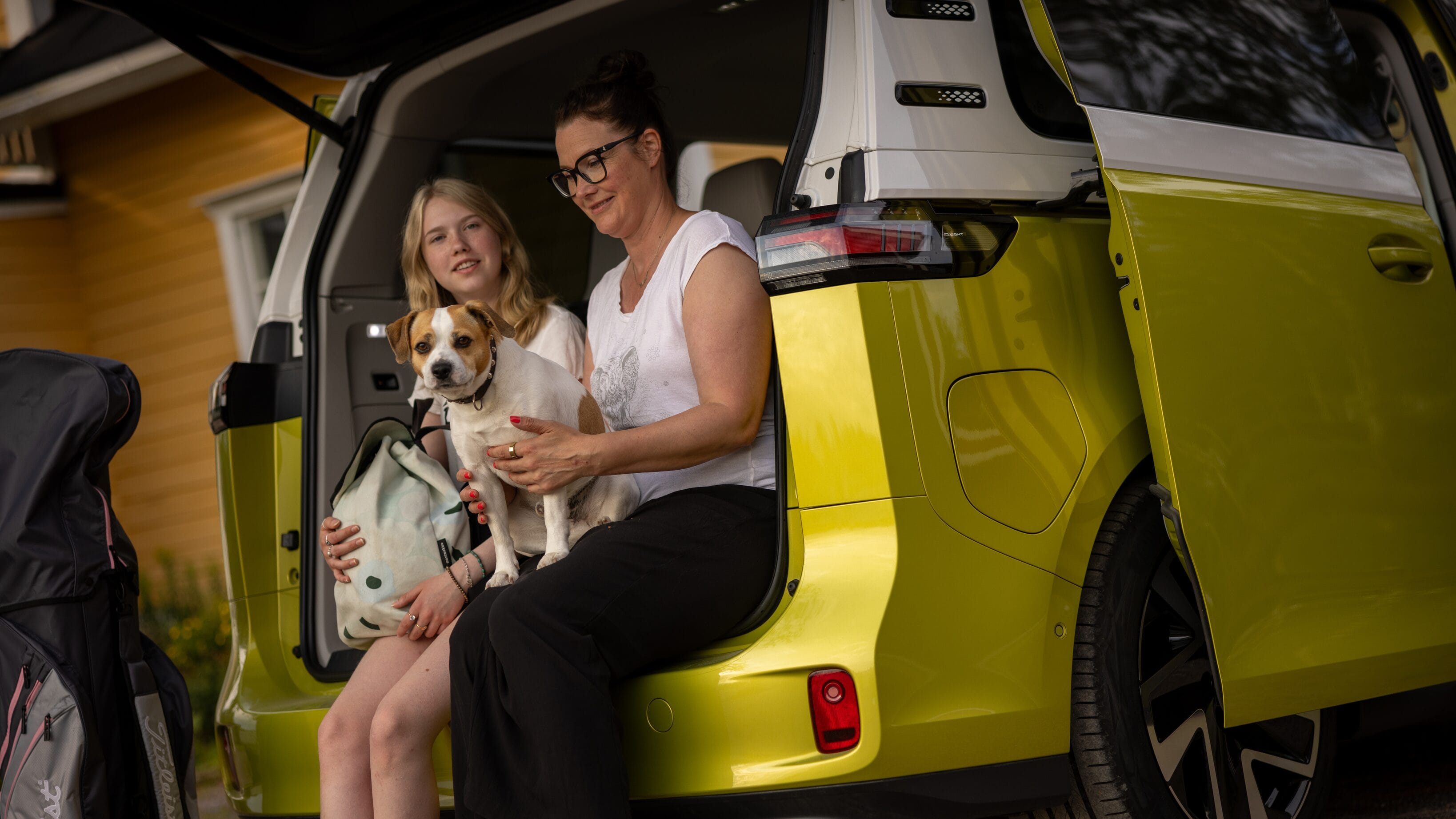 äiti ja tytär auton istuvat tila-auton tavara-tilan reunalla koiran kanssa